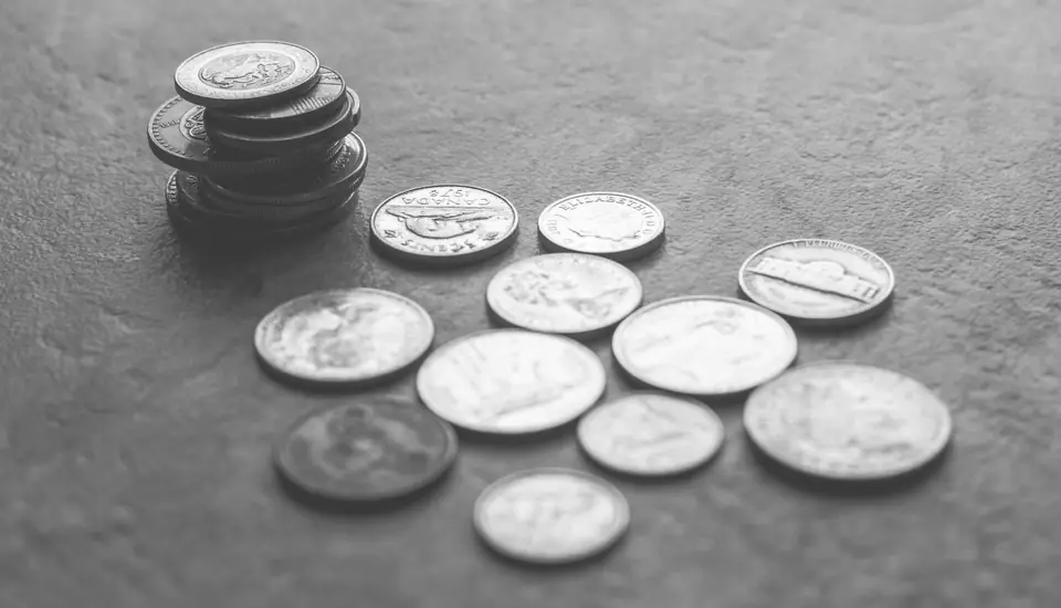 A small stack and a scattered handful of coins lie on a textured gray surface.
