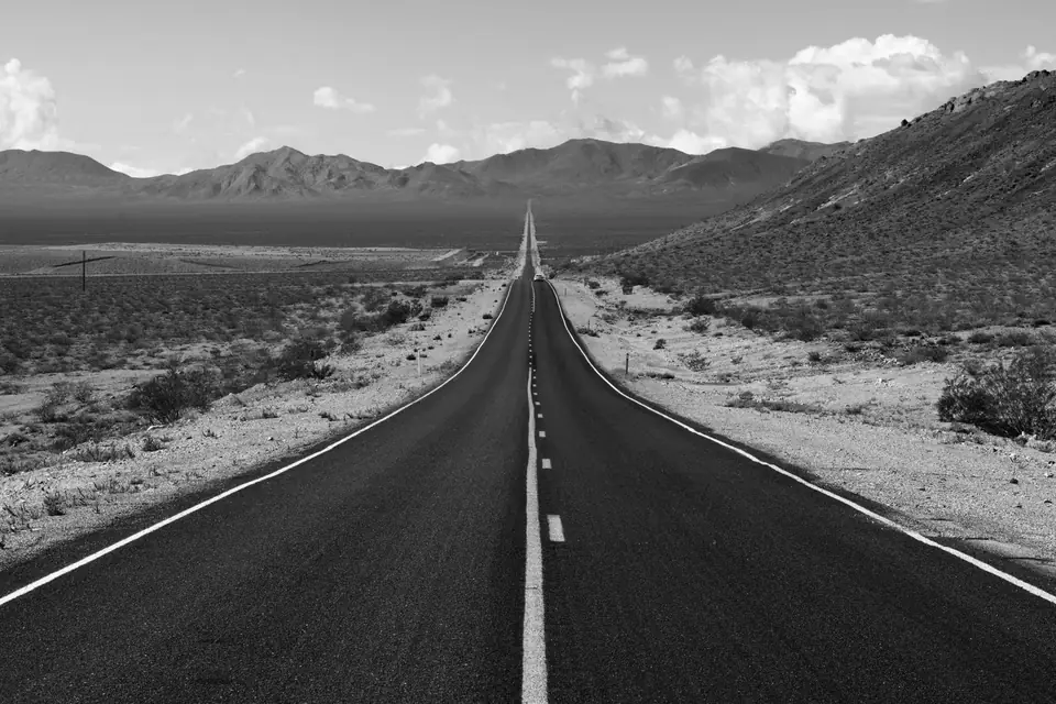 A straight two-lane highway runs through desert scrub toward a distant mountain range.