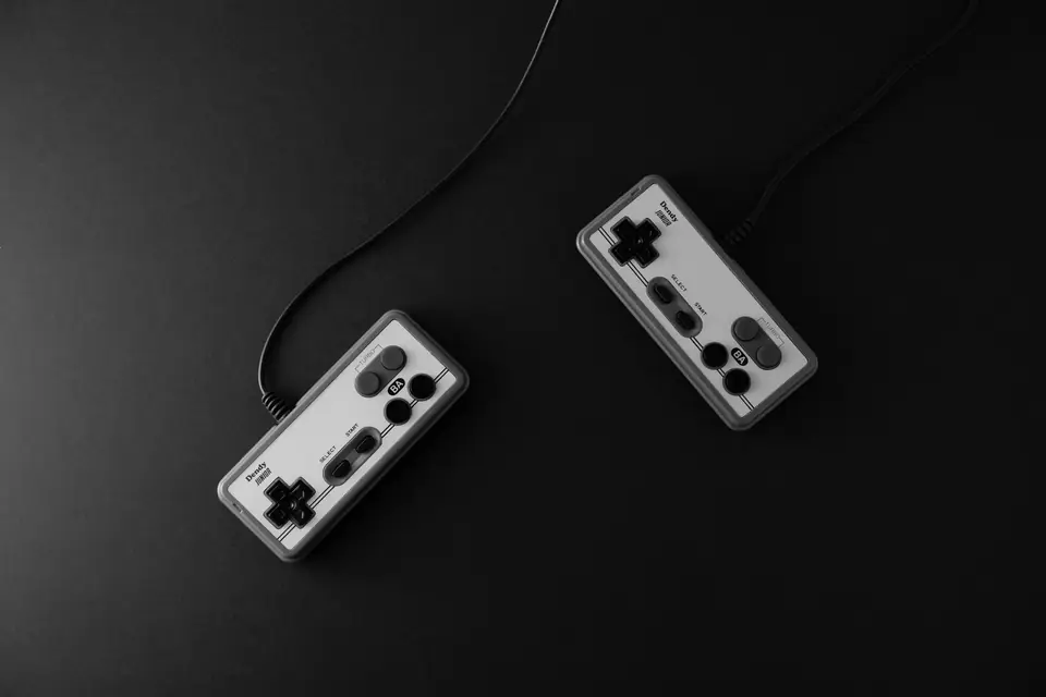 Two light gray game controllers with cords lie apart on a dark tabletop.