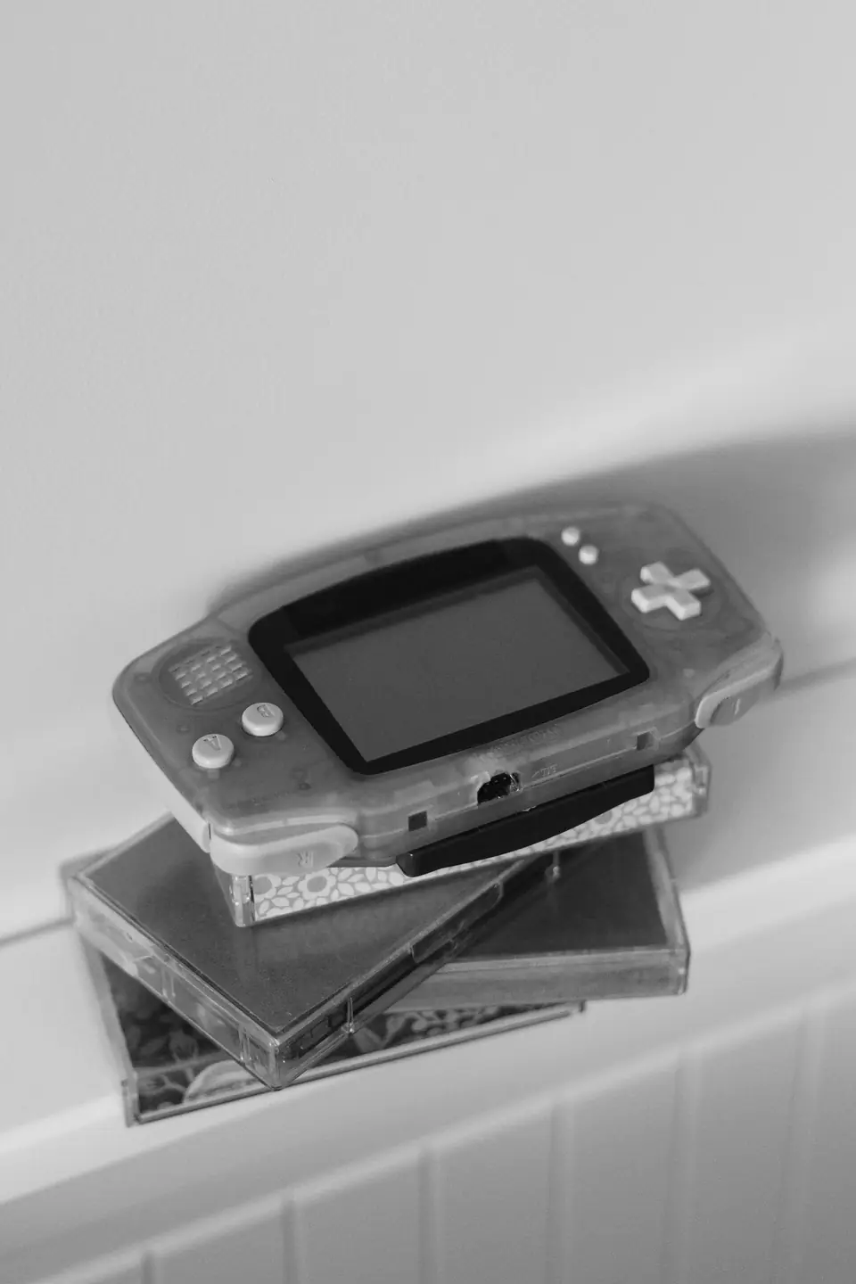 A translucent handheld game console rests on a stack of game cases on a white ledge.