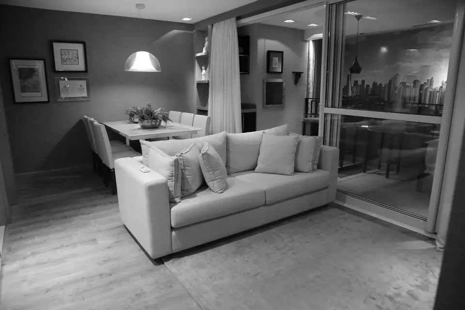 A light sofa with cushions sits near a dining table under a pendant lamp beside glass doors to a balcony.