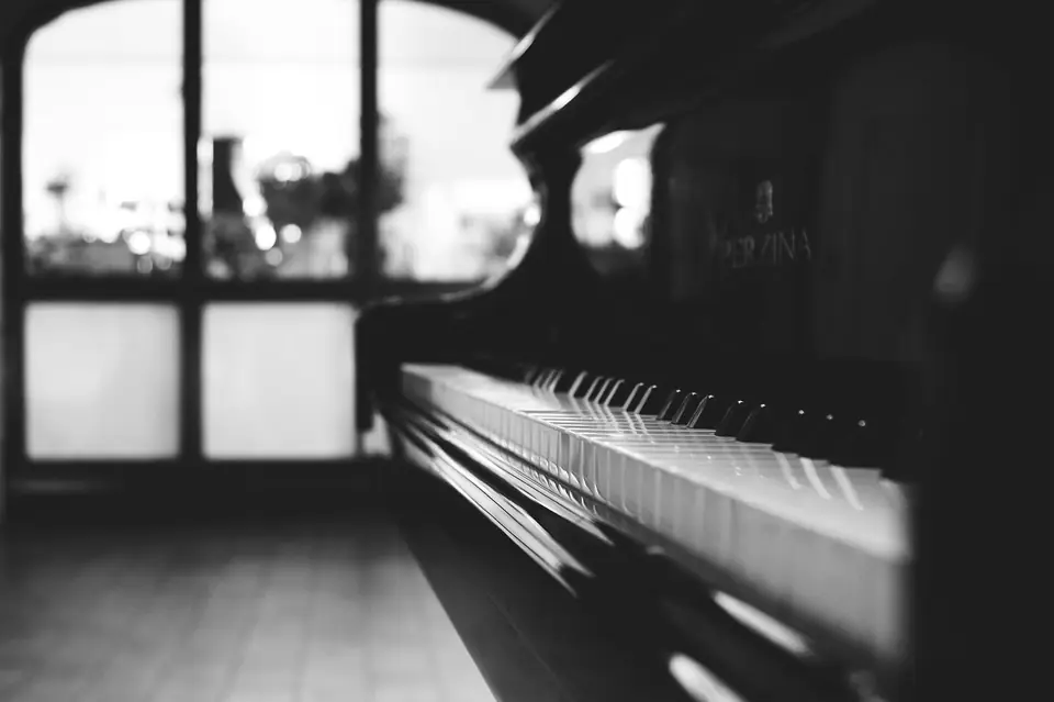 A close view of piano keys receding out of focus toward a bright window.