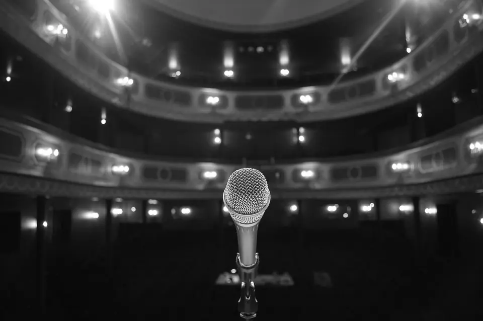 A microphone on a stand faces the balconies of an empty, softly lit theater.