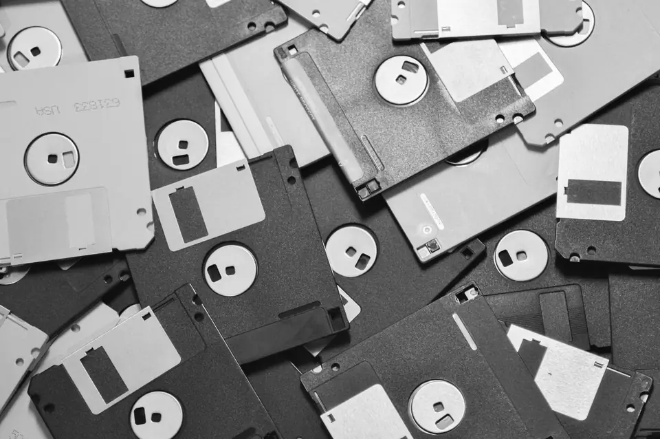 A pile of 3.5-inch floppy disks in light and dark colors lies scattered across a surface.