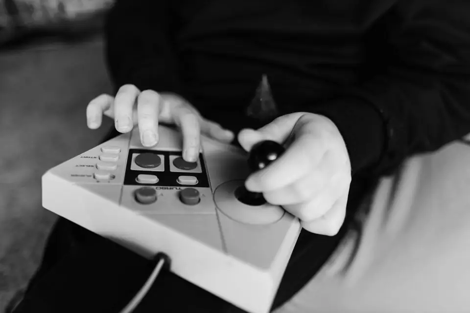 A child’s hands hold a light-colored arcade-style controller with a joystick and several buttons.