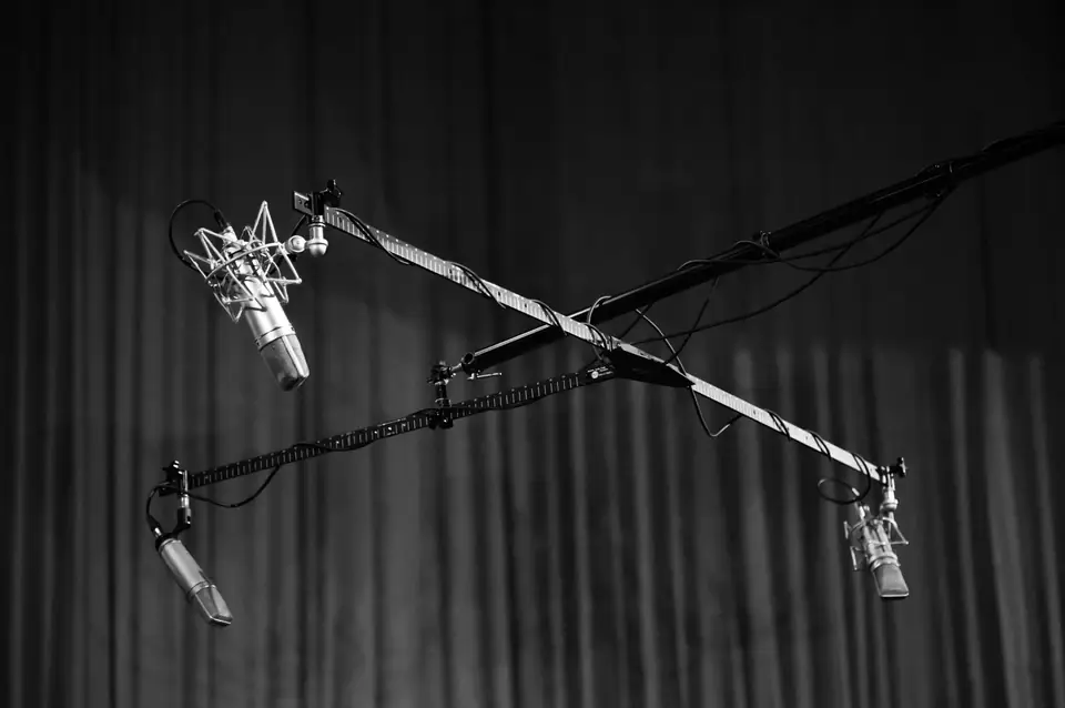 Three studio microphones hang from crossed boom stands in front of a dark curtain.
