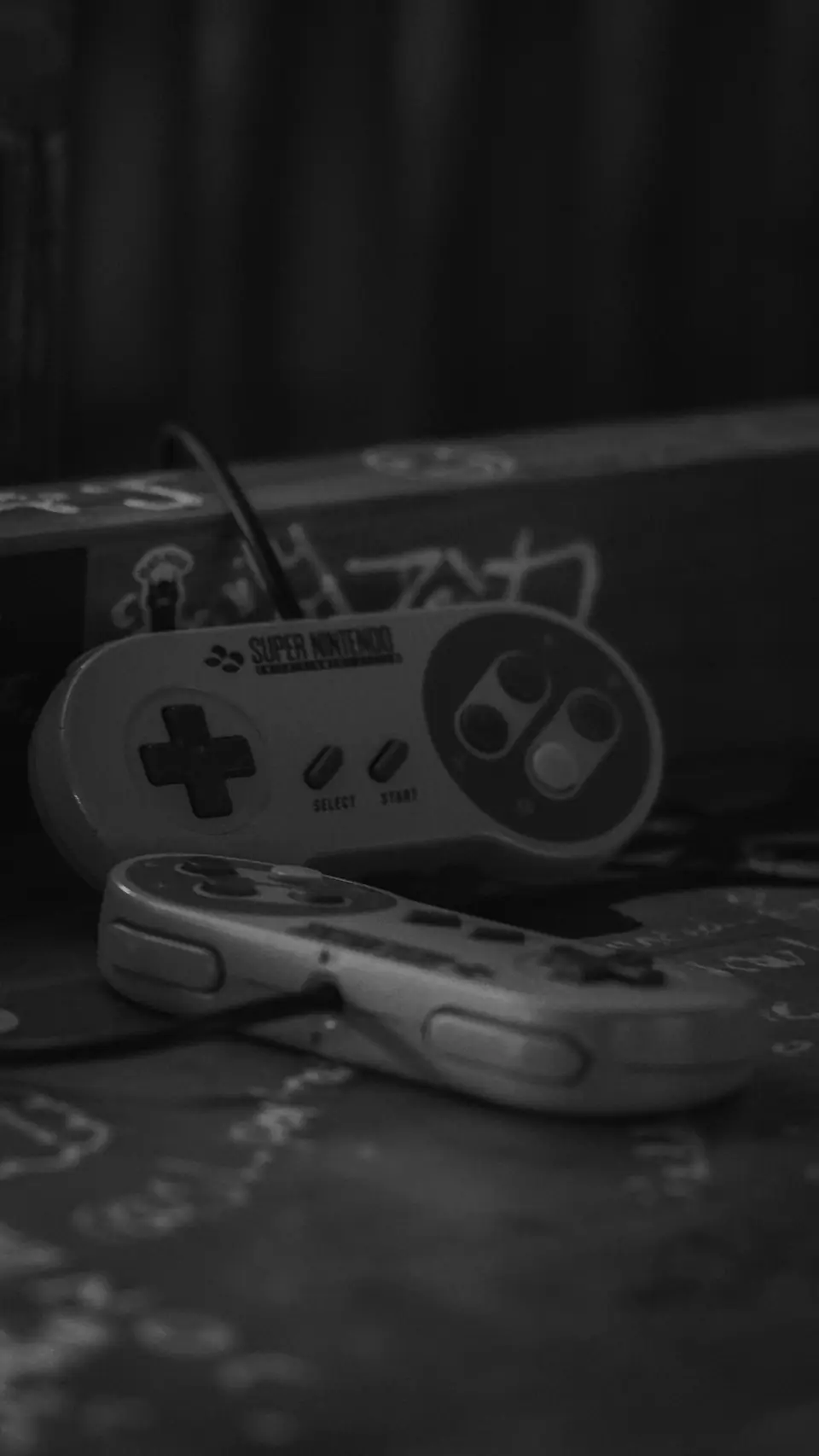 Two Super Nintendo controllers with rounded shapes lie on a box in a dimly lit room.