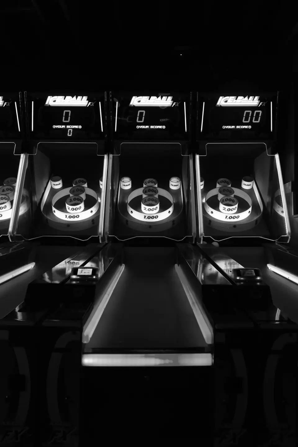 Three illuminated ball-rolling arcade lanes with score displays stand side by side in darkness.