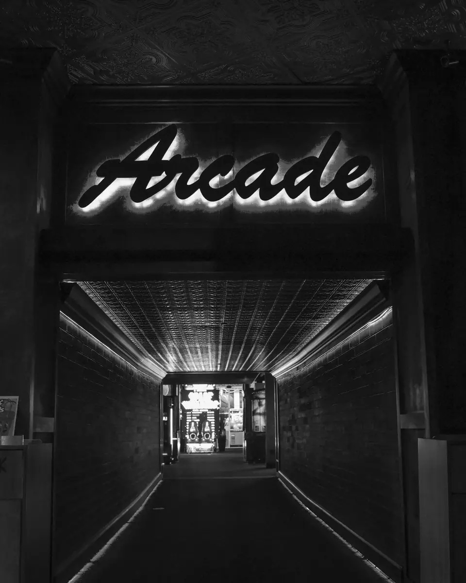 A glowing sign reading “Arcade” hangs above a long, lit corridor leading into a game room.