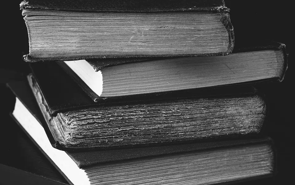 Four worn hardcover books lie stacked on one another against a black background.