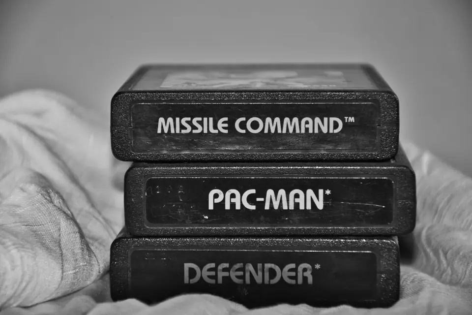 Three stacked video game cartridges labeled Missile Command, Pac-Man and Defender rest on a white cloth.