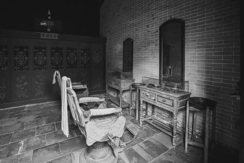 An antique barber chair with a towel draped over it stands in an empty room with brick walls.
