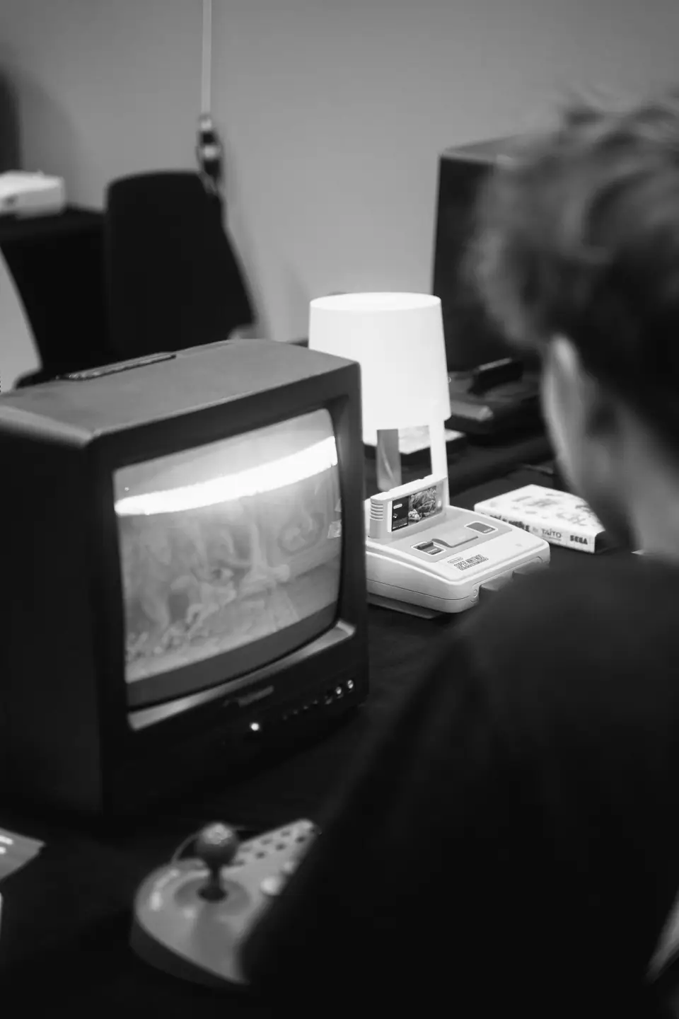A person sits facing a small CRT television showing a game, with a console and a joystick on the table.