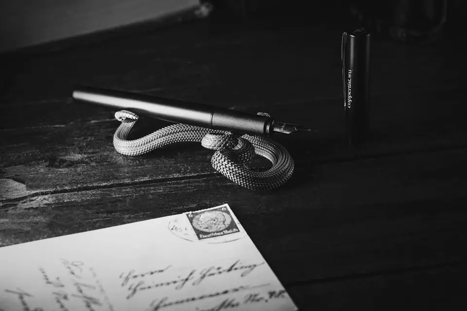 A handwritten, stamped envelope lies on a dark wooden desk near a pen, an ink bottle and knotted cord.