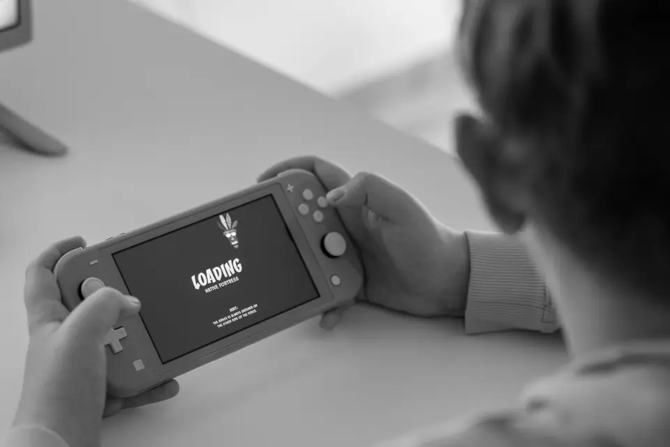 A child holds a handheld game console with the word “Loading” on its screen.
