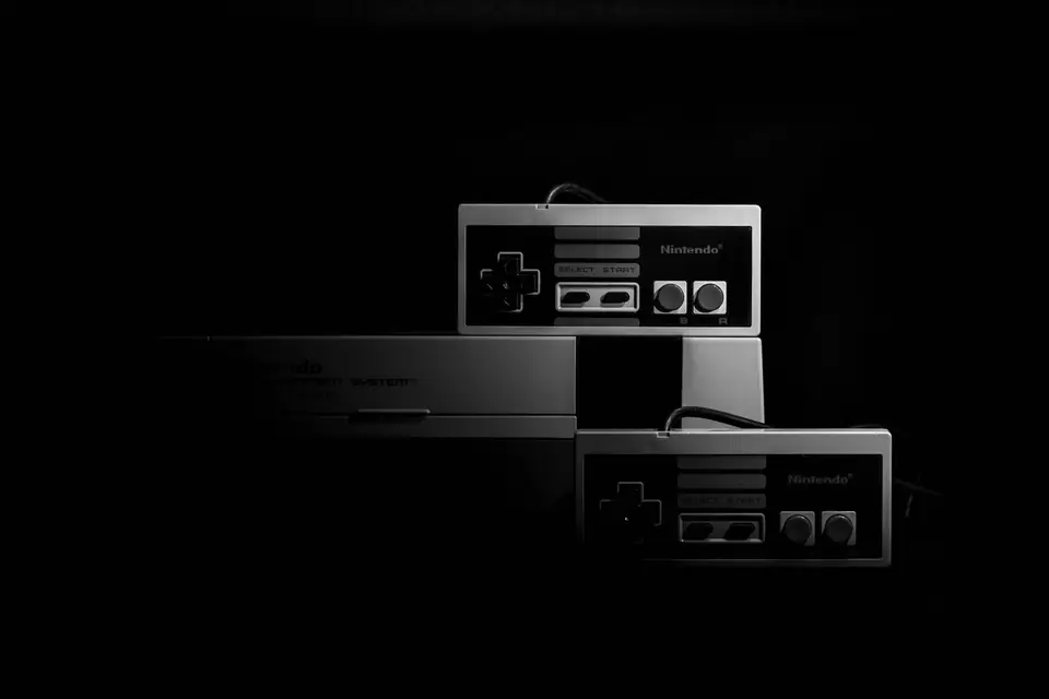 Two rectangular gamepads with direction pads and red buttons rest on a gray console in darkness.