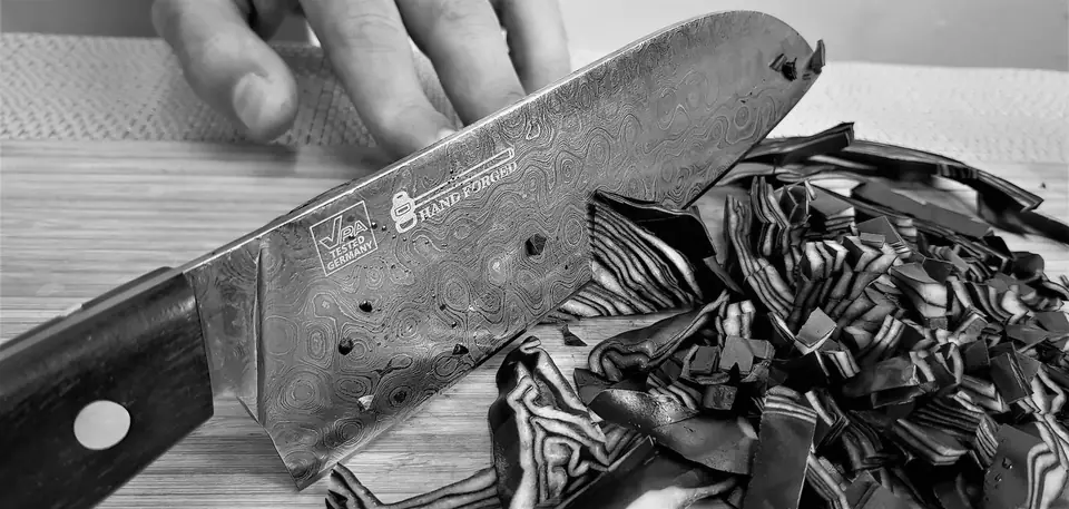 A hand steadies a patterned chef’s knife cutting shredded cabbage on a wooden board.