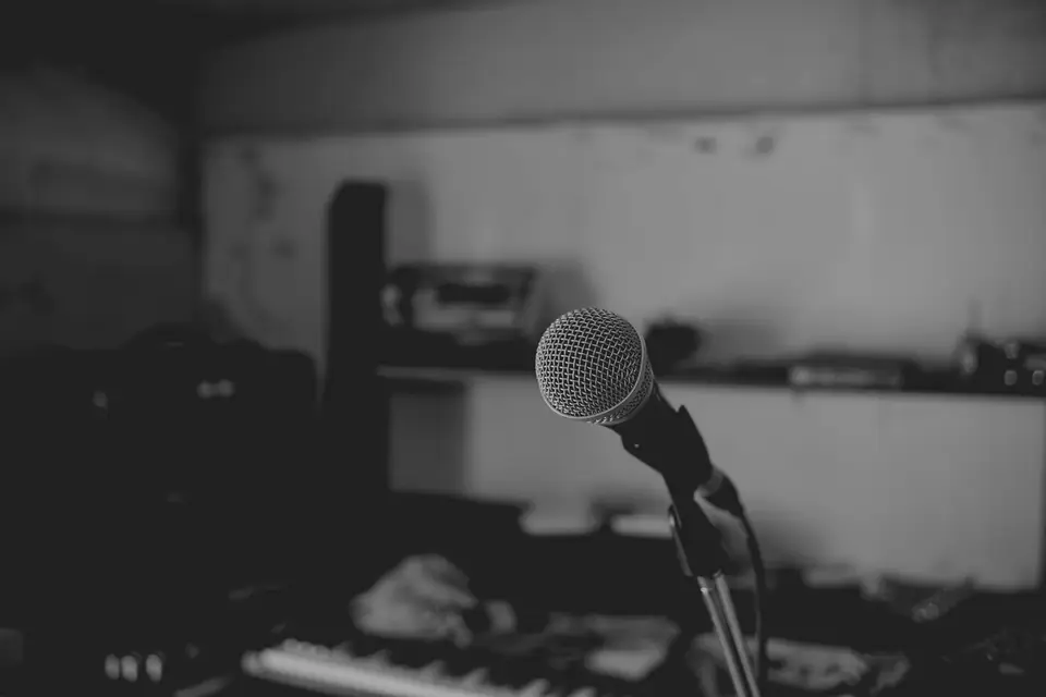 A handheld microphone on a stand faces a dim rehearsal room with a keyboard.