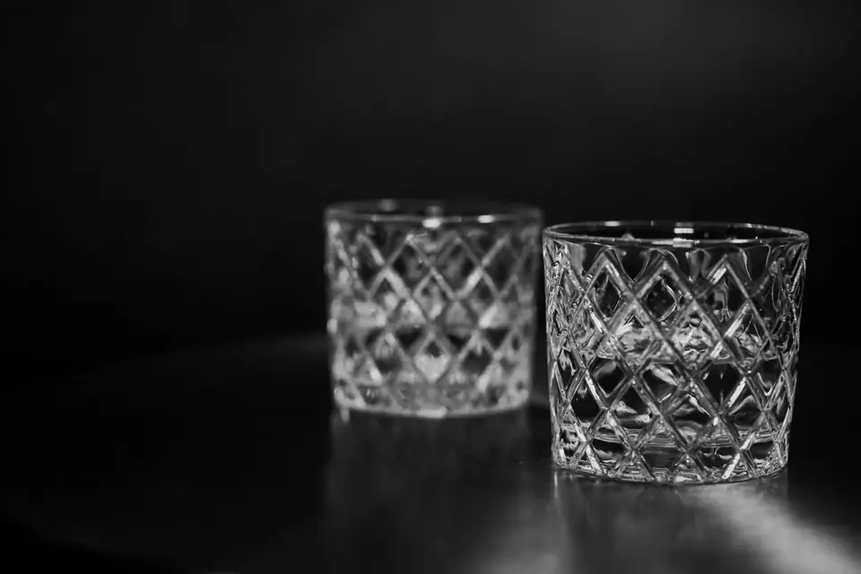 Two empty cut-crystal rocks glasses stand side by side on a dark surface.
