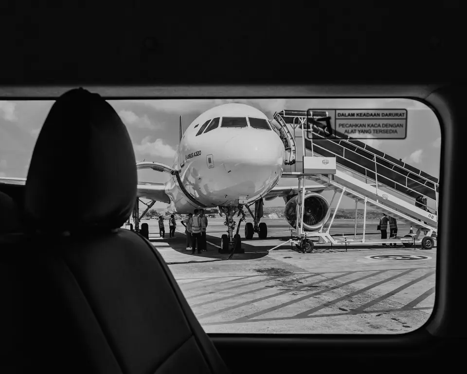 A passenger jet with boarding stairs attached is seen through a car window past a seat headrest.
