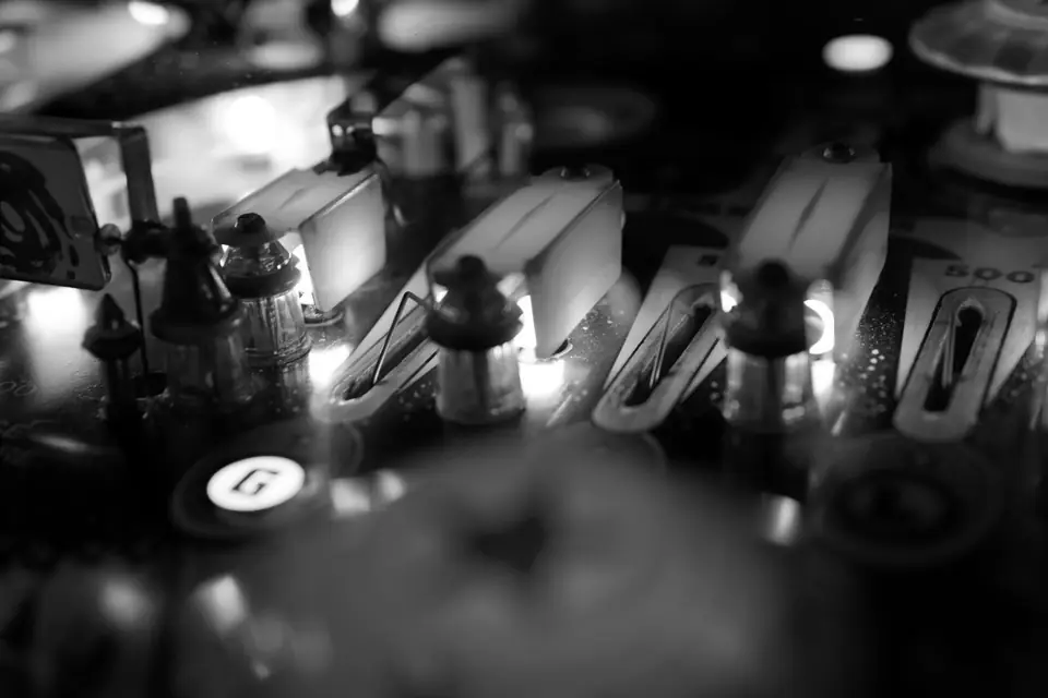 A close view of a pinball playfield shows glowing lights and plastic lane guides behind glass.