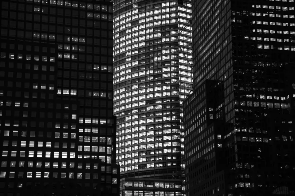 Several tall office towers with many lit windows crowd together at night.