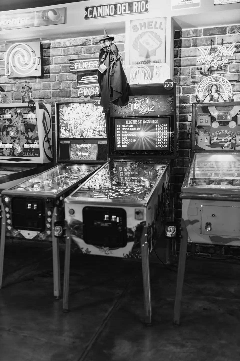 Pinball machines stand in a room with brick walls covered in vintage signs, including a Shell sign.
