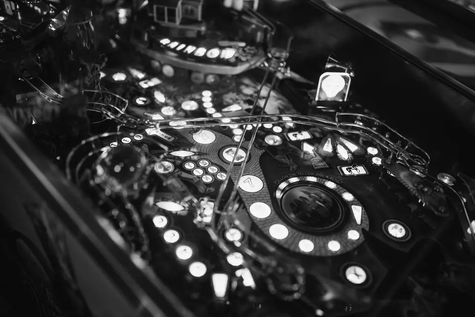 The lit playfield of a pinball machine shows rows of glowing inserts and targets in the dark.