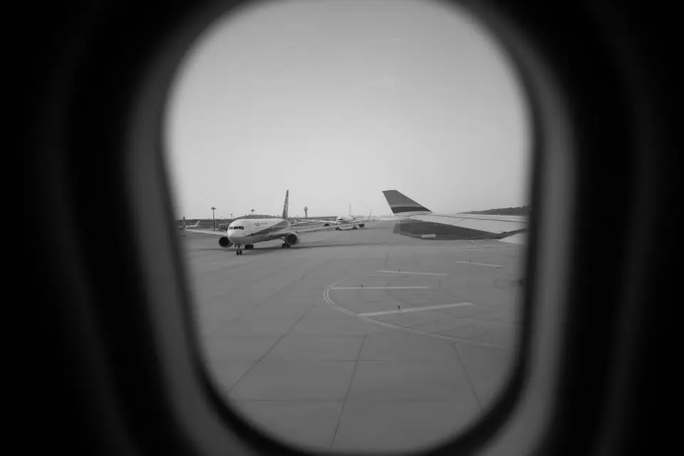Airplanes on an airport tarmac are seen through the oval window of an aircraft cabin.
