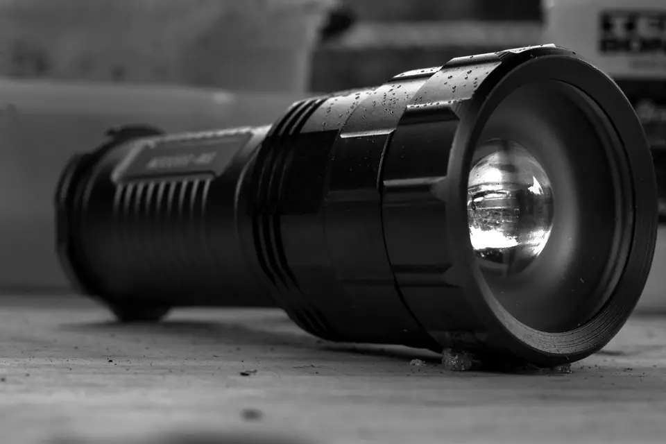 A large black metal flashlight lies on its side on a wooden surface with its lens facing the camera.