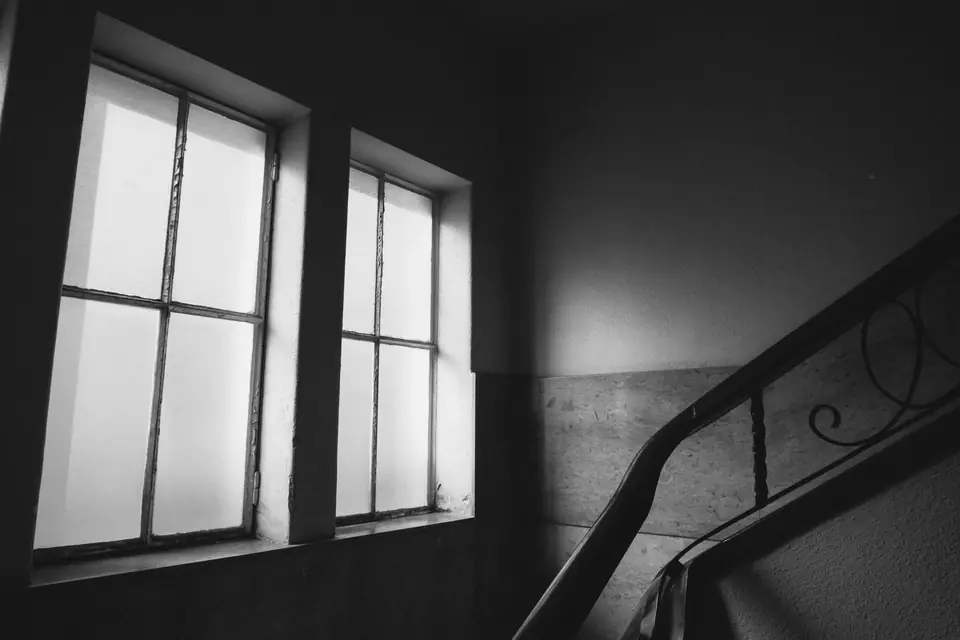 Light from two tall windows falls into an empty stairwell with a curved iron railing.