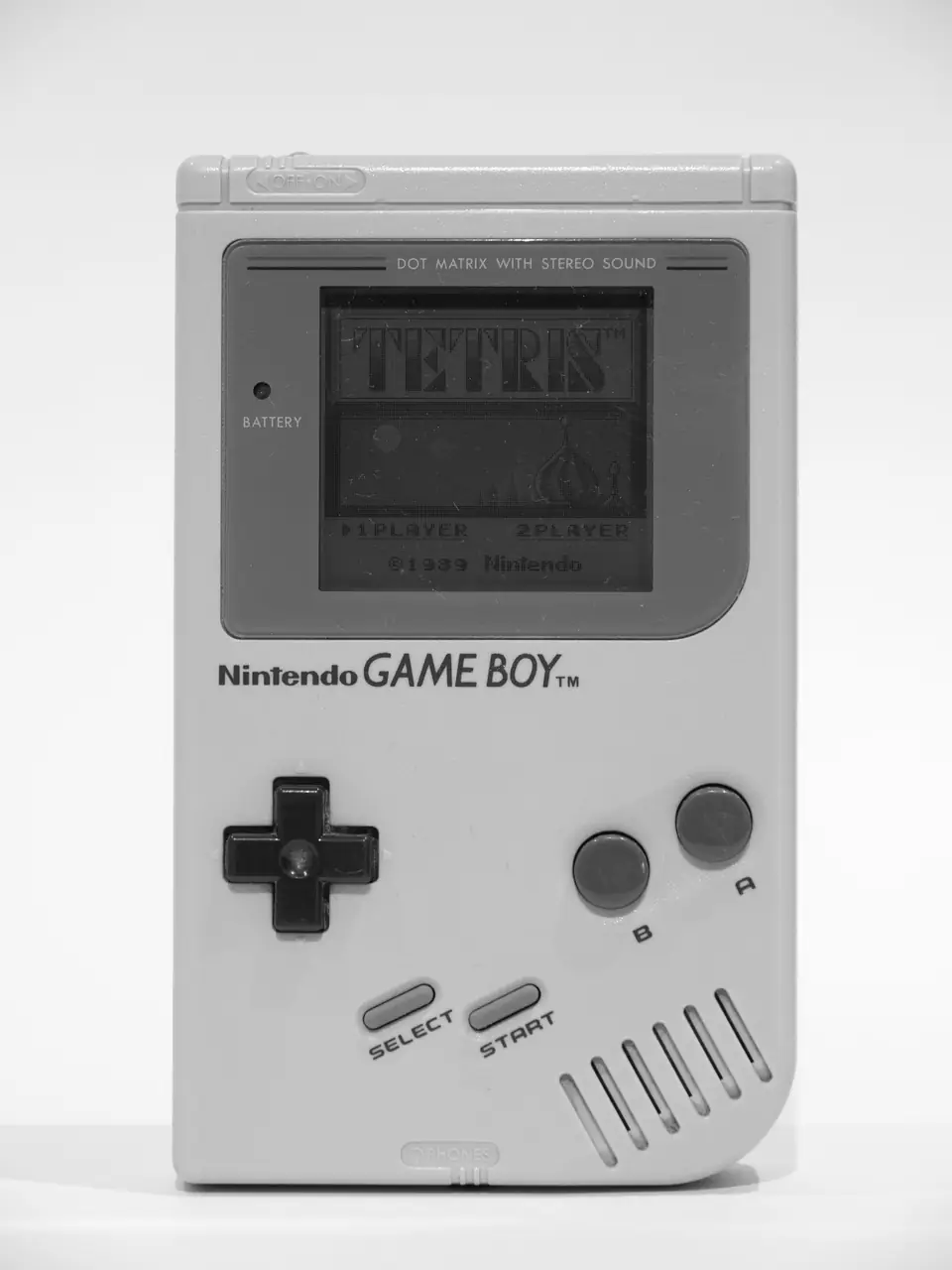 An upright original Game Boy displays the Tetris title screen on its small monochrome display.