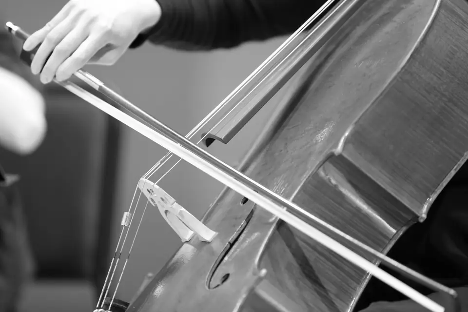 A close view of a hand drawing a bow across the strings of a cello.