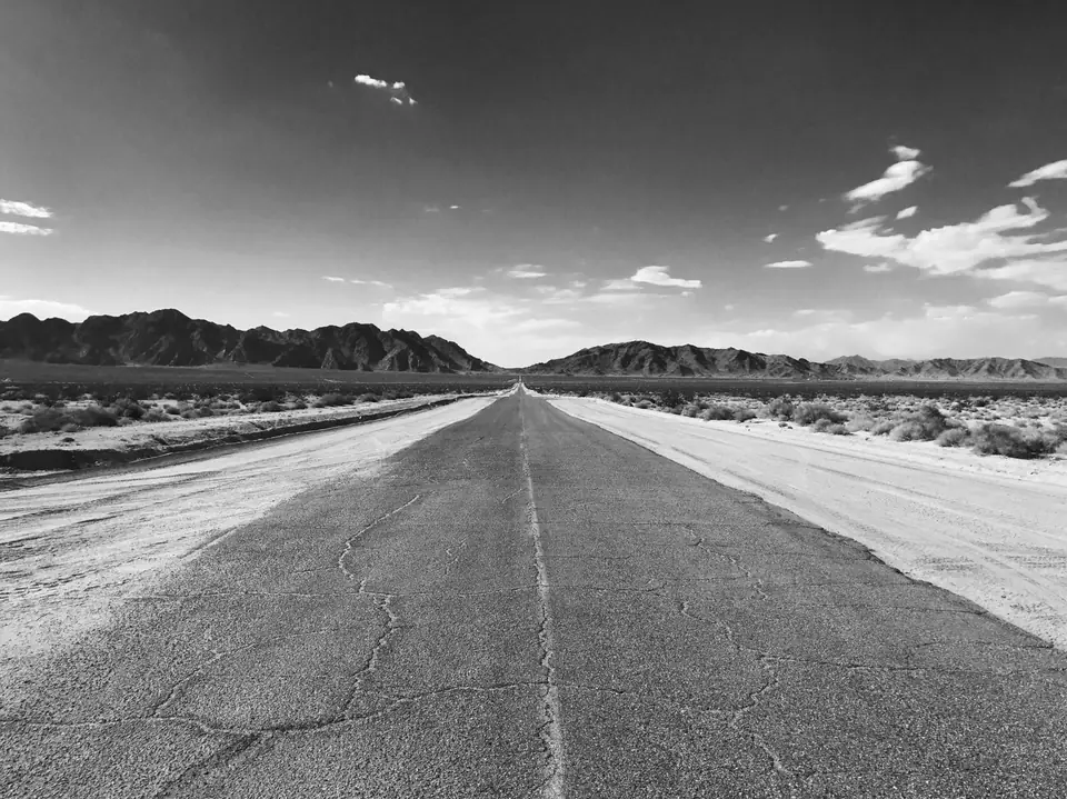 A cracked two-lane desert road runs straight toward low mountains under a bright sky.
