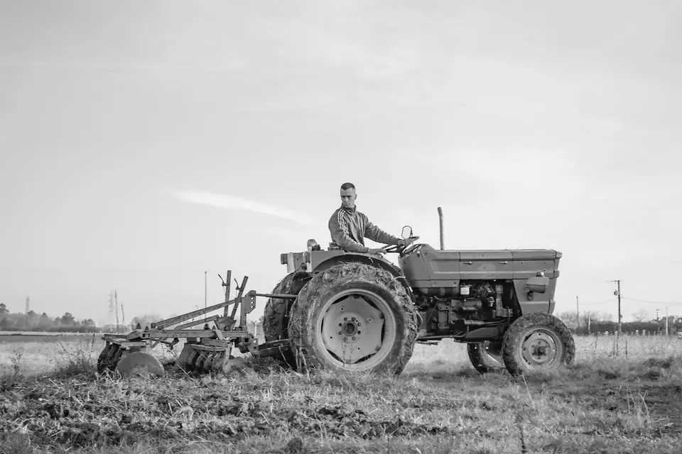 A man drives a tractor pulling a disc harrow across a flat, open field.