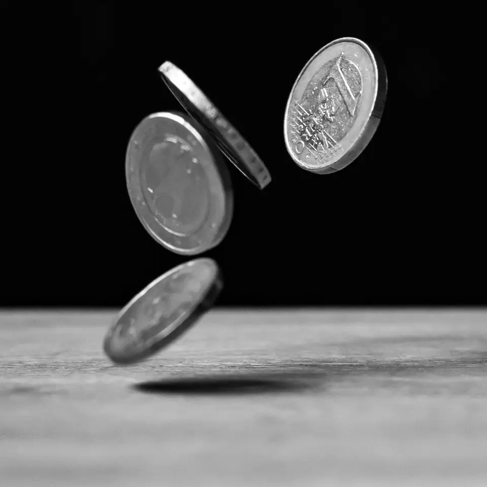 Several coins are frozen in midair as they fall toward a wooden tabletop against a black background.