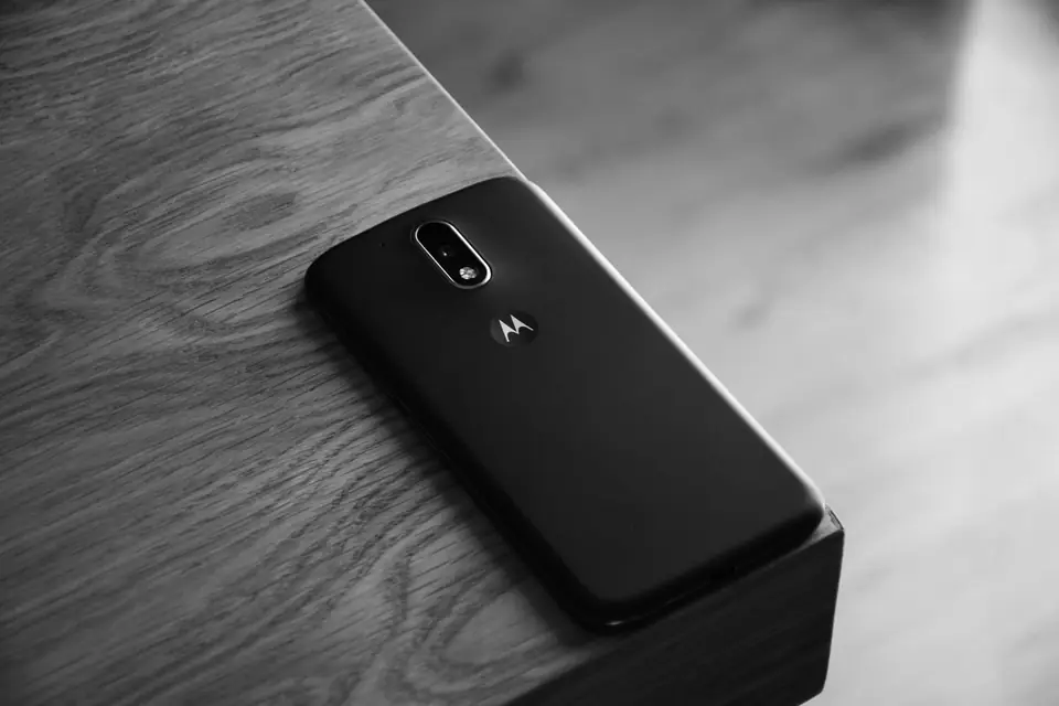 A black smartphone lies face down near the corner of a wooden table.