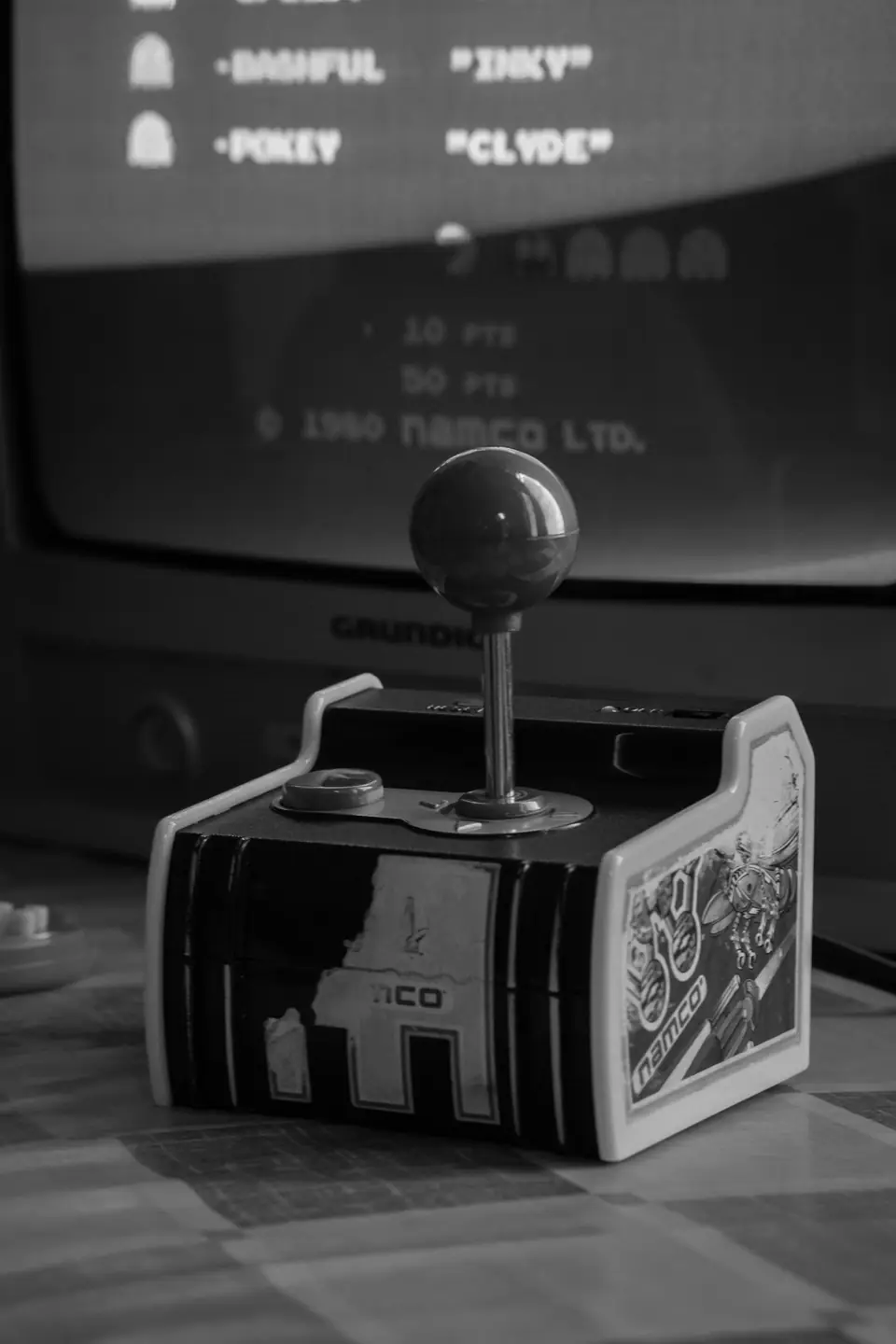 A small tabletop arcade controller with a ball-top joystick sits before a screen listing game characters.