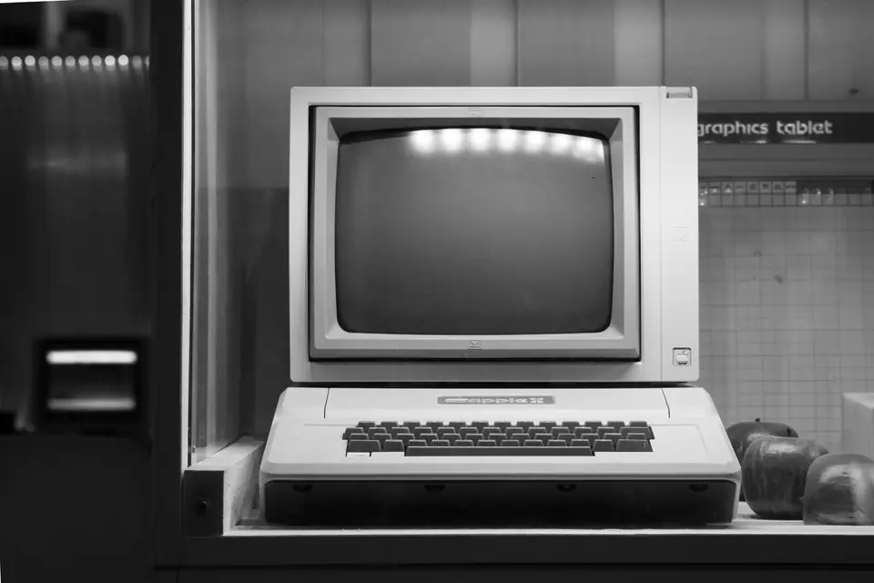 A beige vintage computer with a keyboard and monitor sits inside a glass display case.