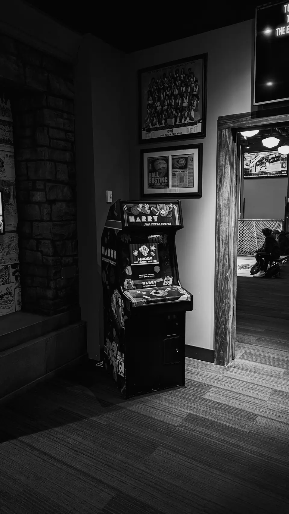 An upright arcade cabinet stands in a dim room near a doorway beneath framed pictures.