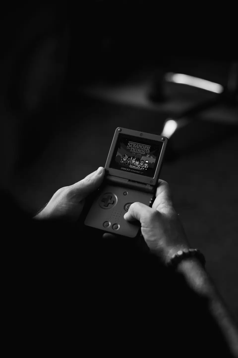 Hands hold an open folding handheld game console with a lit screen in a dark room.