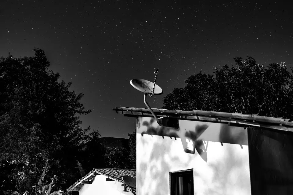 A whitewashed building with a satellite dish stands beneath trees and a starry night sky.