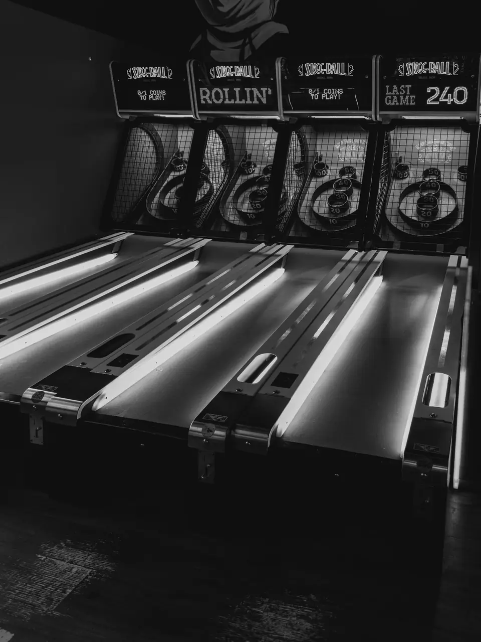Four lit Skee-Ball lanes with scoreboards above them stand in a dark arcade, one display reading 240.
