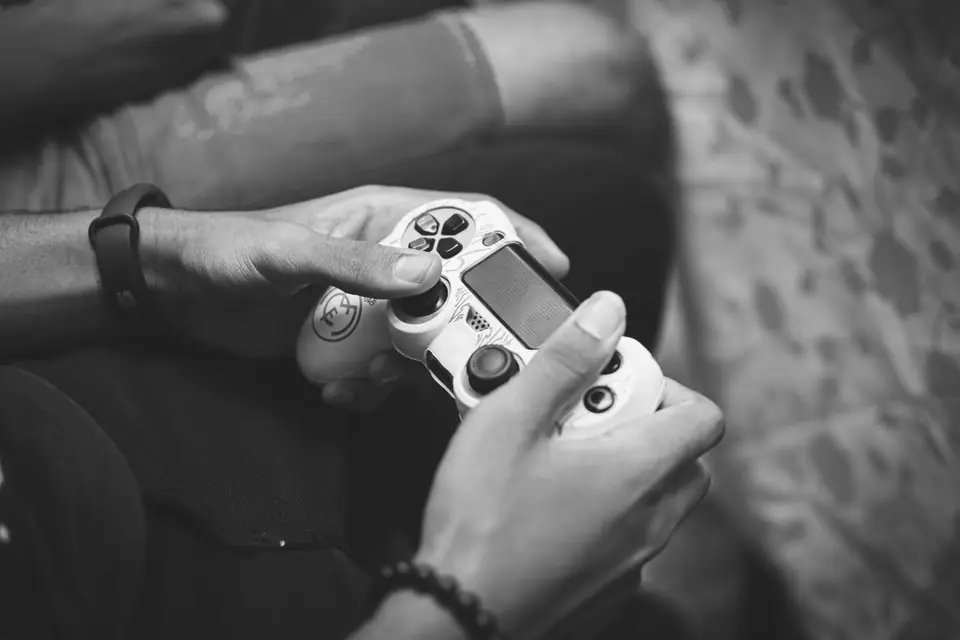 A person’s hands grip a white game controller, thumbs on the sticks and buttons.