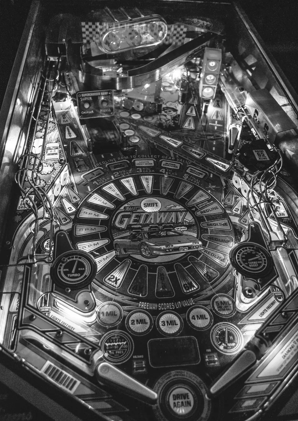 An illuminated pinball playfield with a racing theme is seen from above, showing ramps, lights and flippers.
