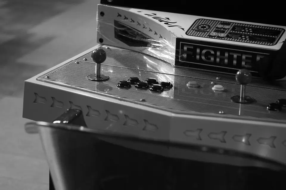 A two-player arcade control panel with joysticks and round buttons sits on a table.