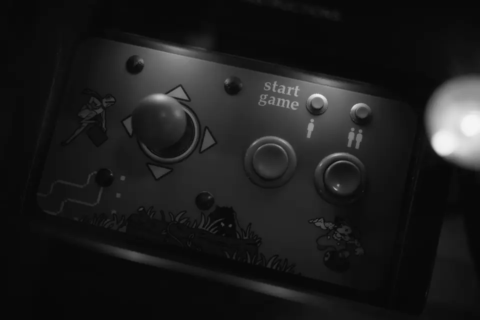 An arcade control panel has a single joystick, two round buttons and cartoon decals in low light.
