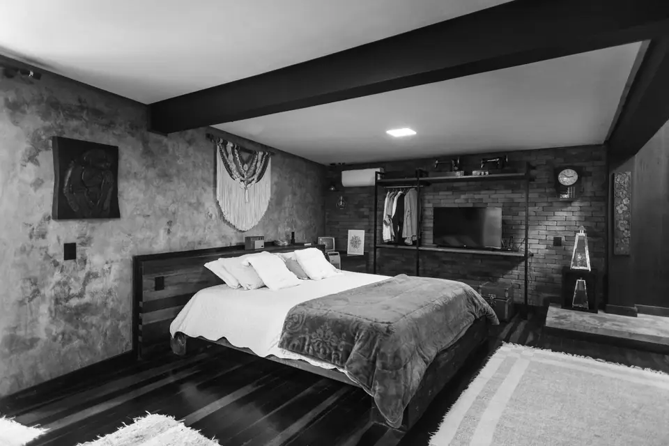 A spacious bedroom with a large bed, a dark ceiling beam, a rug and a television on the far wall.
