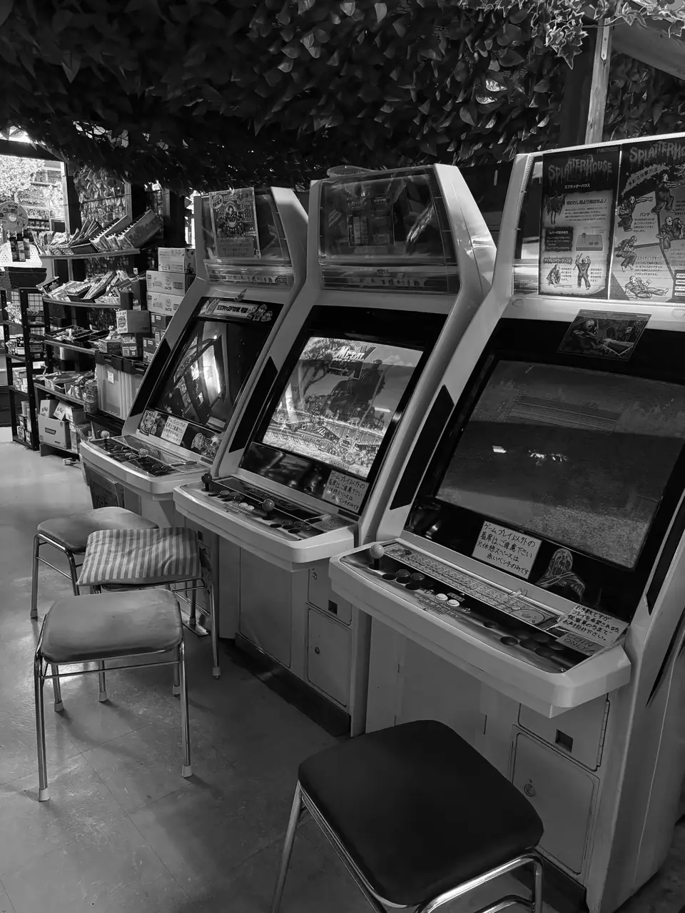 A row of upright arcade cabinets with stools in front of them stands in a narrow game room.