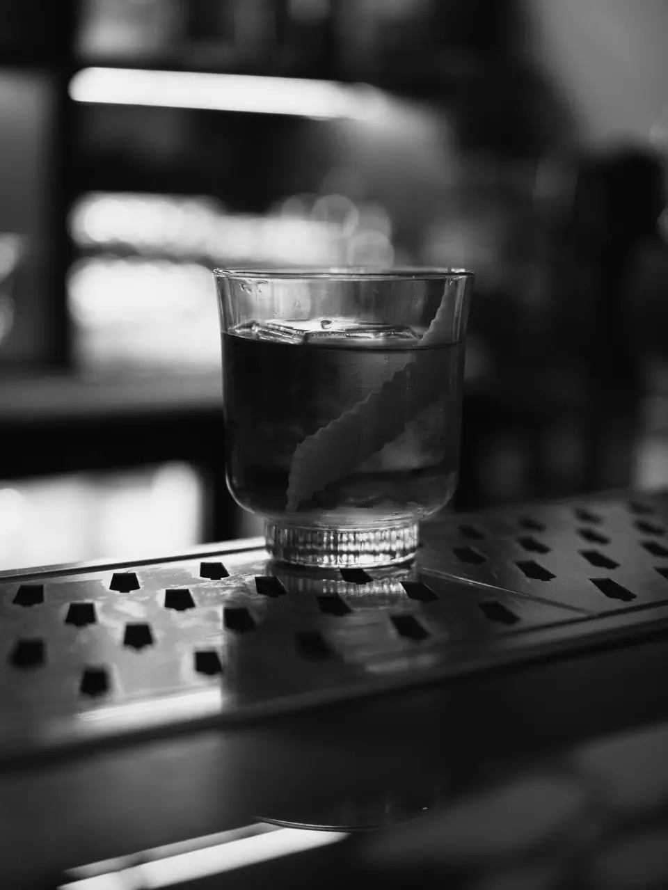 A rocks glass holding a dark drink and a twist of citrus peel sits on a bar mat.